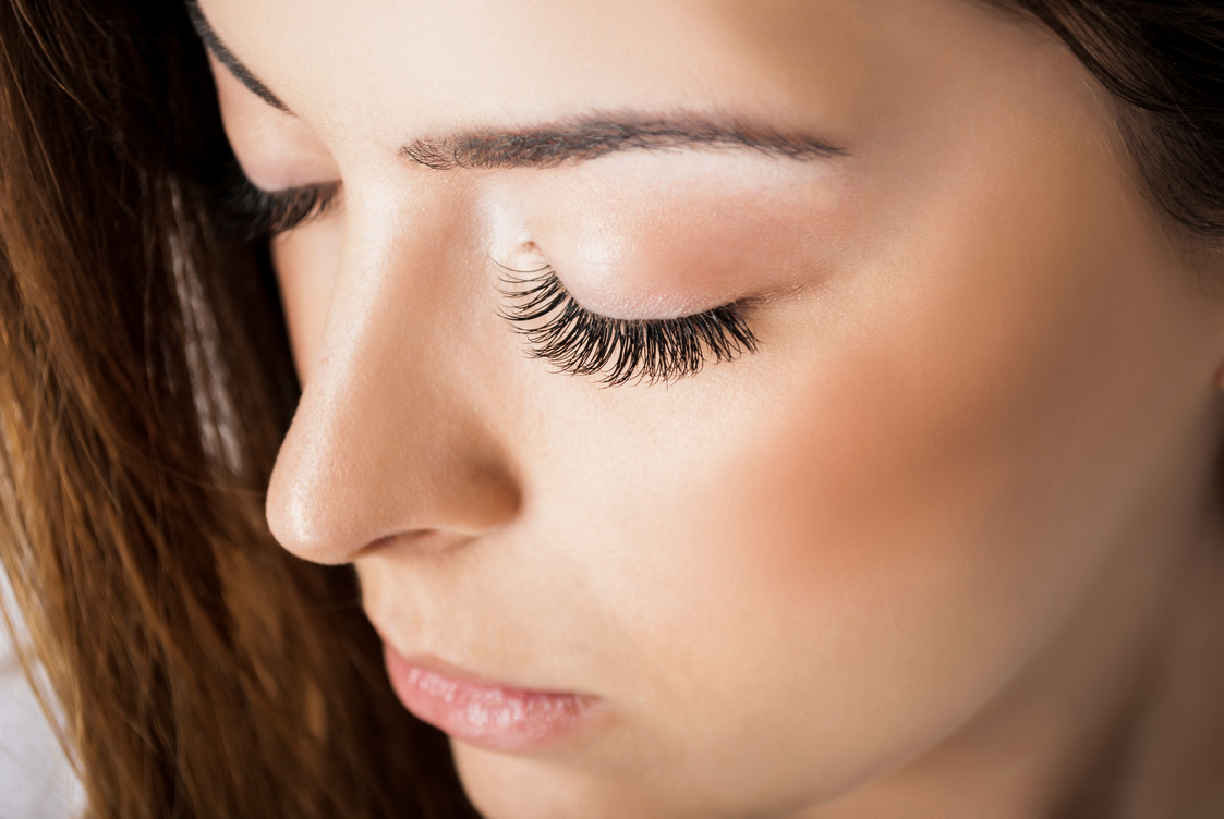 Cute girl with extended silk eyelashes and eyes closed in a beauty studio, close up